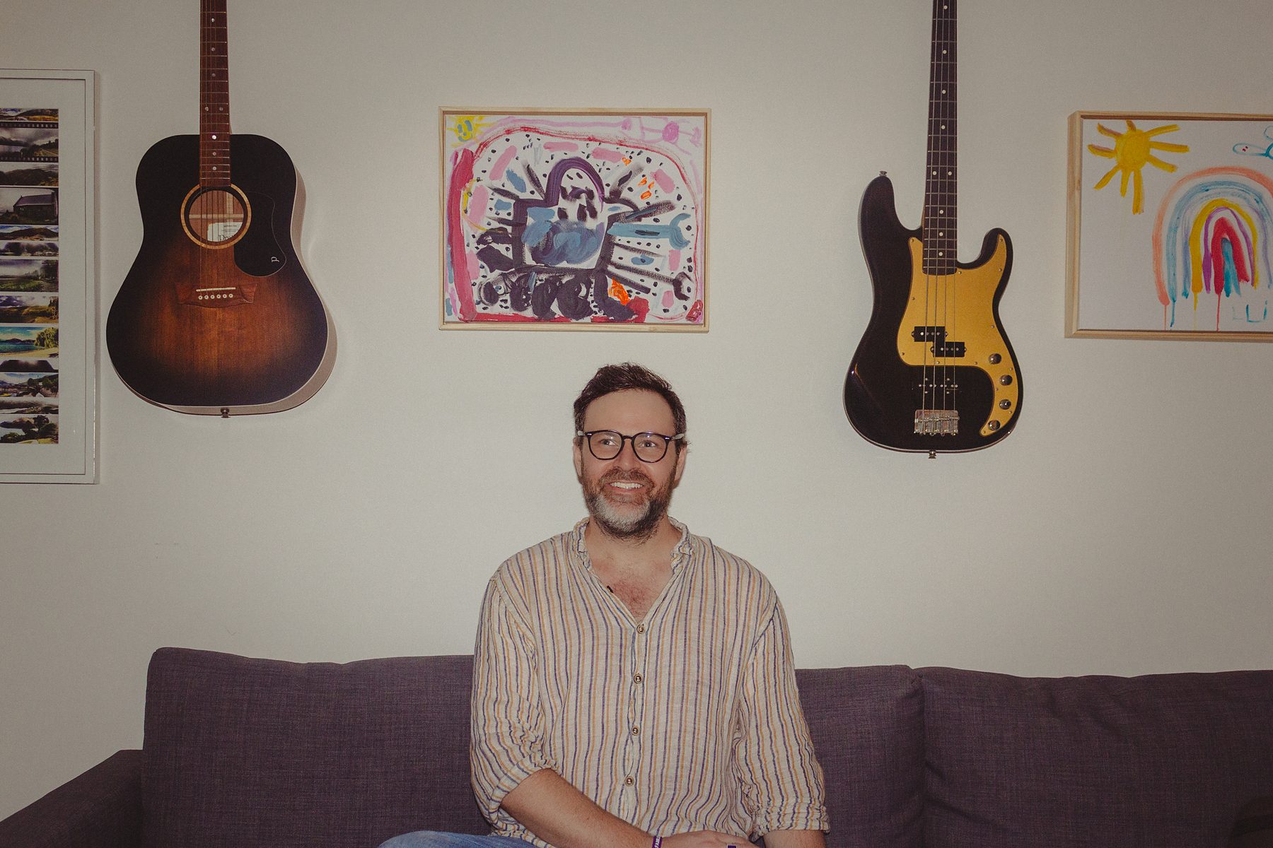 Jack Carty at home, seated on a couch between his guitars mounted on the wall